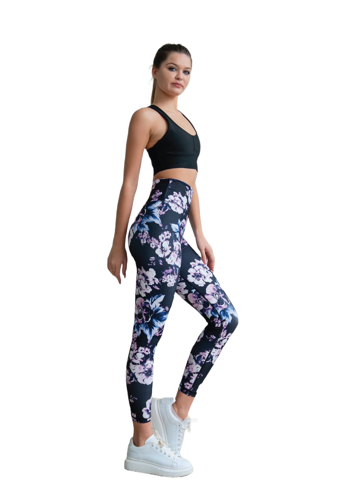 Frau in einem schwarzen Lismina-Sport-BH und 334 High Waist-Leggings mit Blumenmuster, trägt weiße Turnschuhe und posiert vor einem weißen Hintergrund.